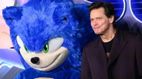 Getty Images Sebuah foto yang diambil pada pemutaran perdana film, memperlihatkan Jim Carrey berdiri di samping seseorang dengan kostum Sonic the Hedgehog biru berbulu raksasa.