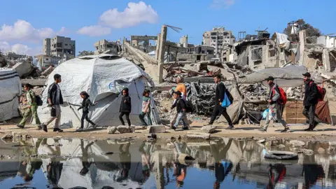 AFP Palestina berjalan melewati kumpulan air oleh tempat penampungan yang didirikan di dekat bangunan yang hancur di lingkungan Nasser di Gaza City (15 April 2015)