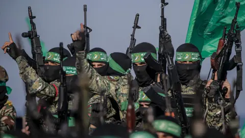 Foto file EPA yang menunjukkan kepada anggota sayap militer Hamas, brigade Izzedine al-Qassam, mengacungkan senjata pada upacara di mana sandera Israel diserahkan ke Palang Merah, di Kota Gaza (1 Februari 2025)