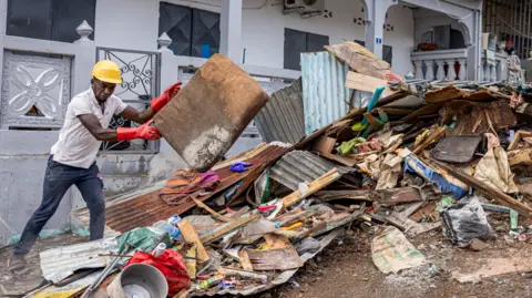 Getty Images Seorang pekerja membersihkan puing-puing di jalan di kota Mamoudzou di wilayah Mayotte di Samudra Hindia Prancis, setelah topan Chido melanda kepulauan itu